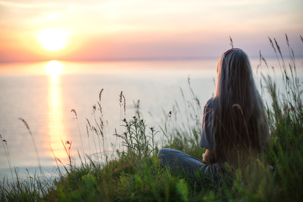 woman sitting on a cliff surrounded by foliage and staring at a large body of water